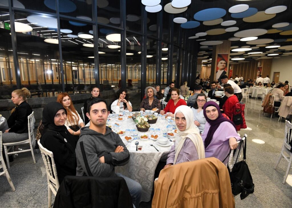 Osmangazi’de düzenlenen Dünya Engelliler Günü programına katılan engelli bireyler ve ailelerinin geniş masa etrafında birlikte görünümü